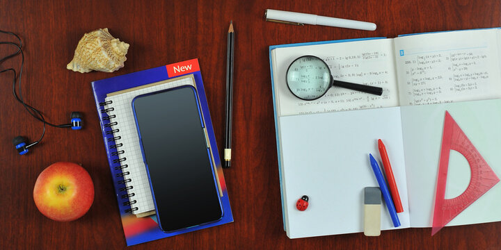 Book, notebook ,lens, smartphone mockup, headphones, apple, pen, pencils on the wooden desk table .Top view, flat lay . Back to school ,education concept.  