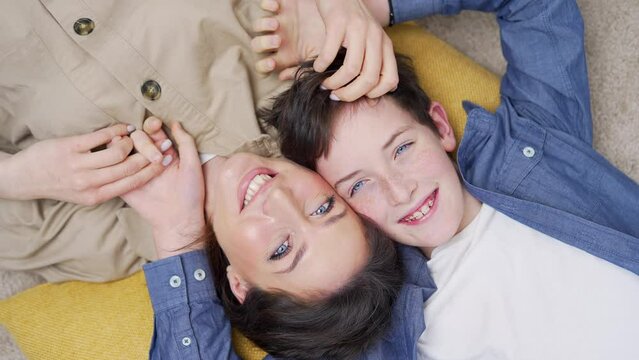 Top view Happy mother and son laughing playing having fun lying on floor at home. Positive emotion and joyful family concept. cheerful mom and kid boy looking at the camera hug together from above