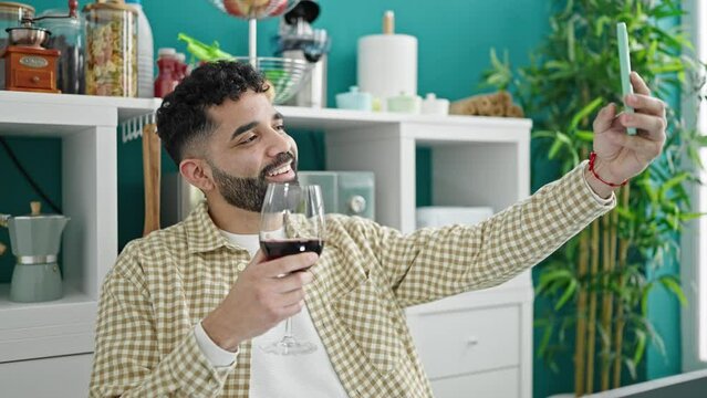 Young hispanic man drinking glass of wine make selfie by smartphone at dinning room