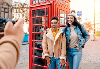 Obraz na płótnie Canvas two friend, girlfriend and women using a mobile phone, camera and taking selfie against a red phonebox in the city of England.Travel Lifestyle concept