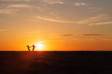 Obraz premium silhouettes of couple at sunset against bright sun sky. man and woman have fun in nature, walking and relaxing, relationships and falling in love. poster postcard romantic meetings against background 