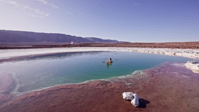 Woman floating alone in turquoise Baltinache salt pools in Atacama desert, Chile. Static shot in slow motion