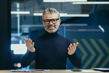 Online psychologist. Senior gray-haired male psychologist, psychotherapist consults with patients remotely via video call. He looks at the camera with a smile, talks amiably.