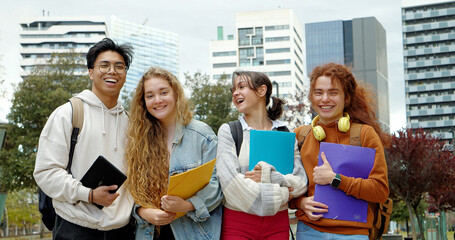 Group of smiling multiethnic teenage students looking at camera with folders and backpacks