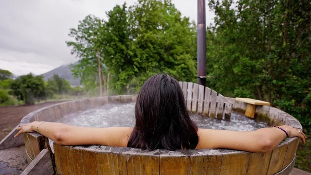 Woman enjoying a hot wood barrel bathtub in the nature at winter. Water steam rising in slow motion.