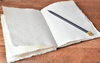 Handmade paper notebook and a simple pencil with a golden crown on a wooden table