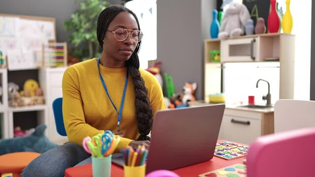 African woman preschool teacher using laptop at kindergarten
