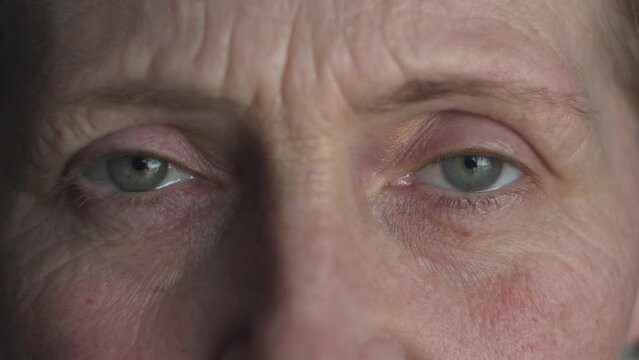 Face of middle aged Millennial woman with natural makeup and green-blue eyes. Beautiful mature female portrait with wrinkles on attractive face opening and closing her eyes. Macro extreme close up