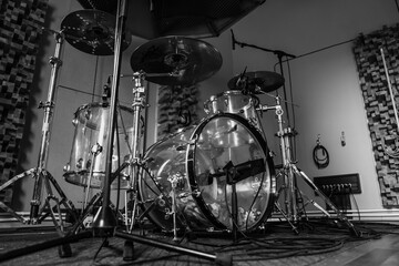 Black and white photo of drum set in record studio with microphones