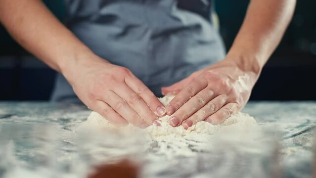 The chef kneads the dough with his hands in the kitchen. Turning flour into dough. Baking pastries, bread and cakes by a professional. High quality 4k footage