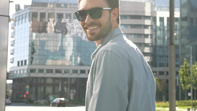Portrait of handsome smiling stylish hipster lambersexual model. Modern man dressed in shirt. Fashion male posing on the street background in sunglasses. Outdoors at sunset 
