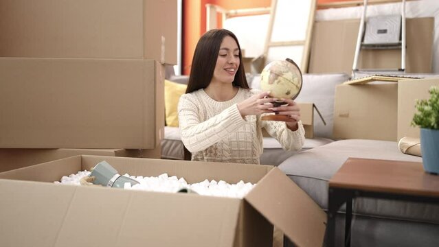 Young beautiful hispanic woman smiling confident unpacking cardboard box at new home