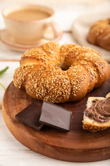 Homemade sweet bun with chocolate cream and cup of coffee on a white wooden. side view, selective focus.