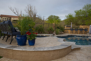 A desert landscaped backyard in Arizona featuring a travertine tiled pool deck, spa and outdoor kitchen.