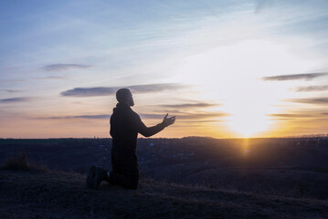 A man with raised hands is praying. On the background of the sunset sky. Repentance for sins....