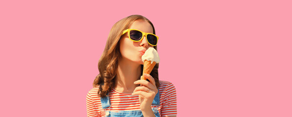 Summer portrait of happy young woman eating ice cream wearing sunglasses on pink background