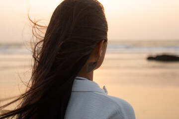 Closeup rearview headshot of brunette long haired woman in in white shirt contemplate at seawater horizon and sunset sky