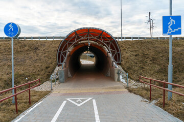 A modern bike path with markings and road signs. The bicycle road runs through a tunnel through a busy highway. A recreation area in the park and places for bicycles.