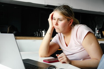 Young woman is working at home online, she is sitting concentrating on working on laptop. Fatigue and burnout. Problems of modern woman. Loneliness and life crisis. Freelance.