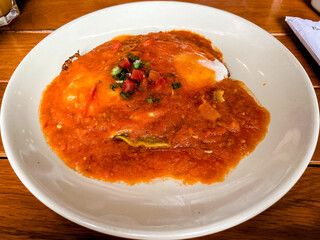 drowned eggs in red sauce on a white plate on a wooden table