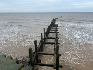 Wooden breakwater on the shore of the sandy beautiful beach at Overstrand Norfolk East Anglia scenic view out to horizon across ocean in cloudy weather.