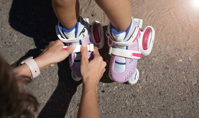 Close-up Mother putting on inline skates rollers to daughter child in public park in summer. Family...