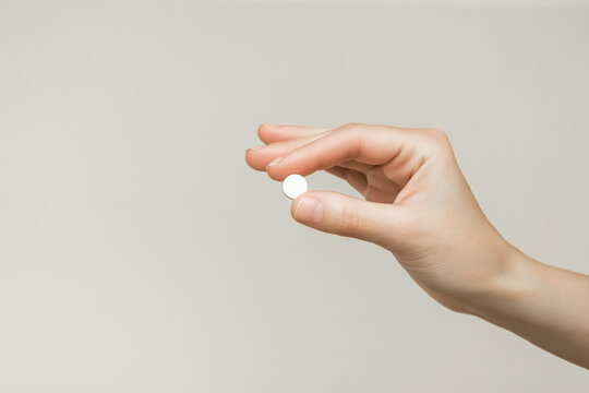 Female Hand Holding A Round White Pill On A Gray Background