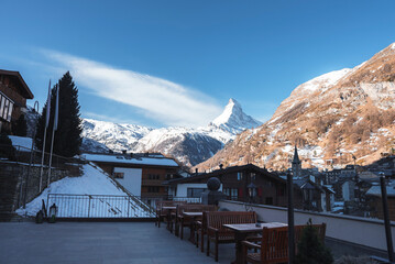 Clock tower and buildings in town in front of beautiful snow covered majestic mountains with sky in background at Zermatt, Switzerland, winter holiday travel concept