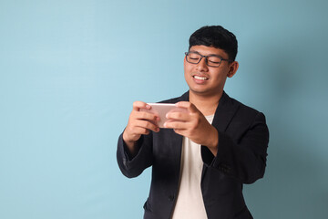 Portrait of young Asian business man in casual suit with big smile looking at phone. Isolated image on blue background