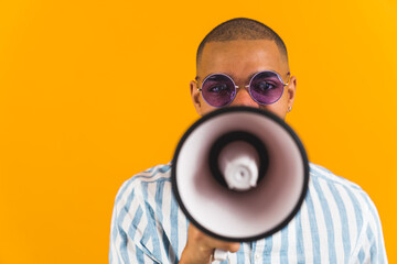 Front view of a man hiding his face behind a megaphone on orange background. High quality photo