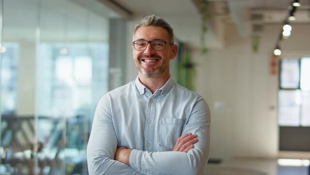 Camera tracks across smiling mature businessman wearing glasses standing in modern open plan office looking into camera - shot in slow motion - Powered by Adobe
