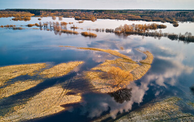 Spring flood rural landscape. Trees, meadow, bushes, fields, country road under High Water inundation. Sky, clouds reflection in evening light. Freshet Overflow aerial view. Floodplain area. - 593096769