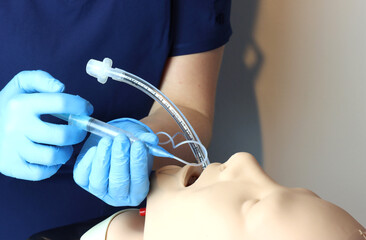 Inflating the endotracheal tube cuff with a syringe with air. Health care professional with gloves and surgical scrubs inflating the cuff