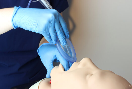 Laryngeal mask airway (LMA) Bering inserted in a simulated patient airway by a health care professional wearing gloves and surgical scrubs 