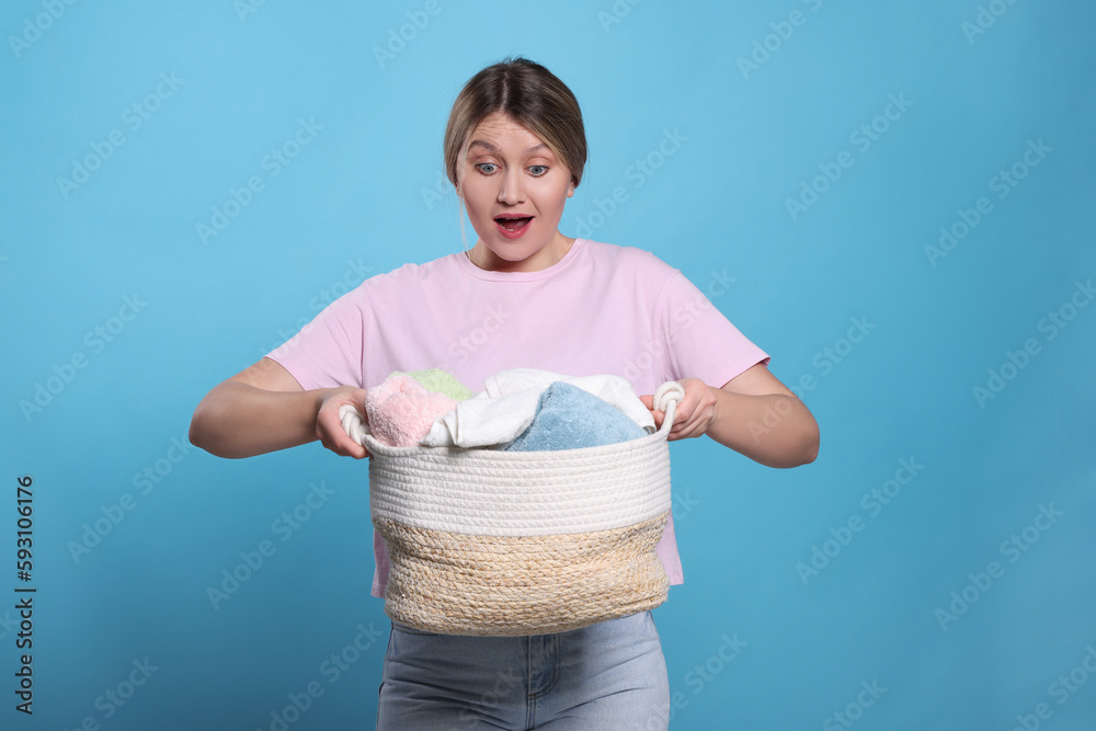 Wall mural Emotional woman with basket full of laundry on light blue background