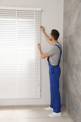 Fototapeta na wymiar Worker in uniform opening or closing horizontal window blind indoors
