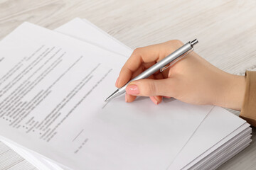 Woman signing document at wooden table, closeup