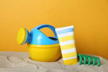 Suntan product and plastic beach toys on sand against yellow background
