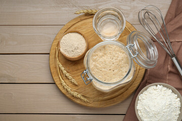 Leaven, ears of wheat, whisk, water and flour on beige wooden table, flat lay