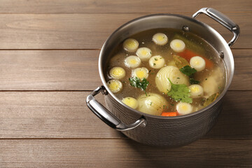 Pot with tasty bouillon on wooden table, space for text