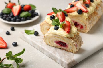 Tasty meringue roll with jam, cream, strawberry, blueberry and mint on light grey table, closeup