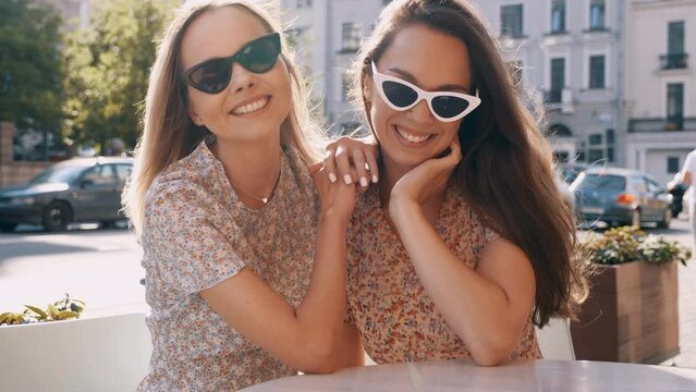 Two young beautiful smiling hipster female in trendy summer dresses  clothes. carefree women posing in the street. Positive models having fun at sunny day. Cheerful and happy. In sunglasses