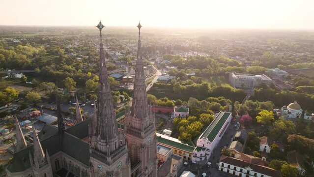 video a&eacute;reo orbital 4k, de torres de antigua catedral con la ciudad de fondo al atardecer, lujan, buenos aires, argentina