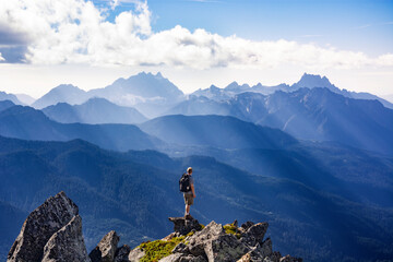 Adventurous athletic male hiker standing on top of a rugged mountain in the Pacific Northwest with...