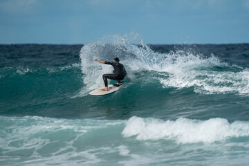 Caucasian male surfer black wetsuit surfing wave cutback surfboard ocean blue
