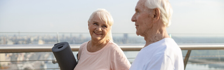 Sportive mature woman and man stand on bridge in modern city at sunset light