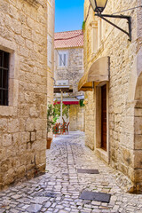 Fototapeta na wymiar Narrow street with stone houses. Old houses and old narrow alley in Trogir, Croatia, Europe. Streets in old town.