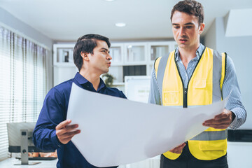 Competent investor investor discuss and brainstorm with engineer on blueprints, construction plans before putting them into action. Professional establishing investment plan for engineering projects.