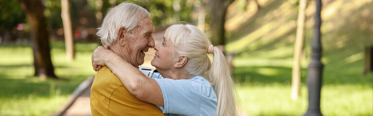 Sportive senior wife and husband embrace standing on road in park