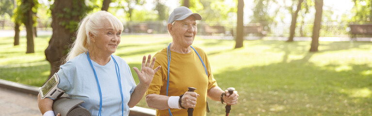 Positive senior woman with mat and man with poles for Nordic walking in green park
